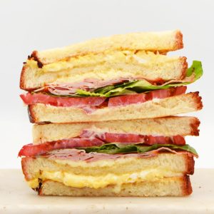 Club Sandwich with toasted bread, omelette, lettuce, tomato, ham, cheese, mayonnaise, and hollandaise sauce